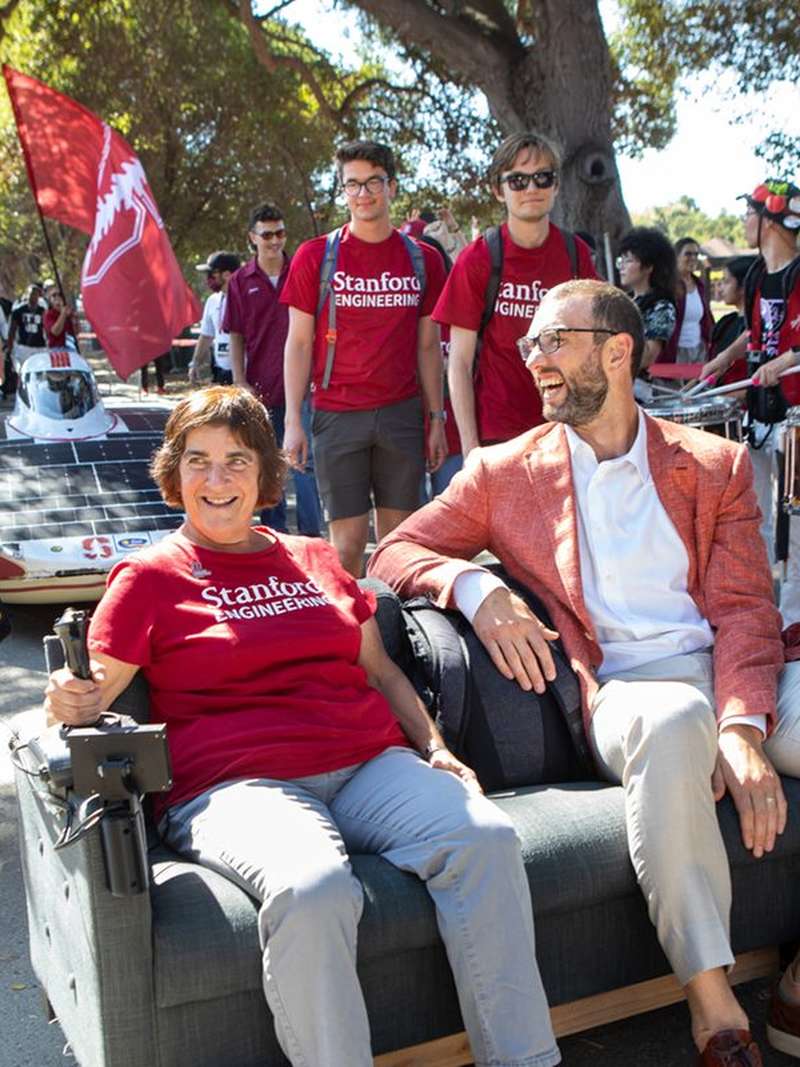 Former provost Persis Drell and Andrew Luck ride a motorized couch through campus.