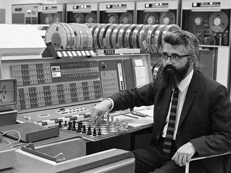 Professor John McCarthy shows off computer chess in 1966, sitting in front of a furniture-sized computer with reel to reel tapes.