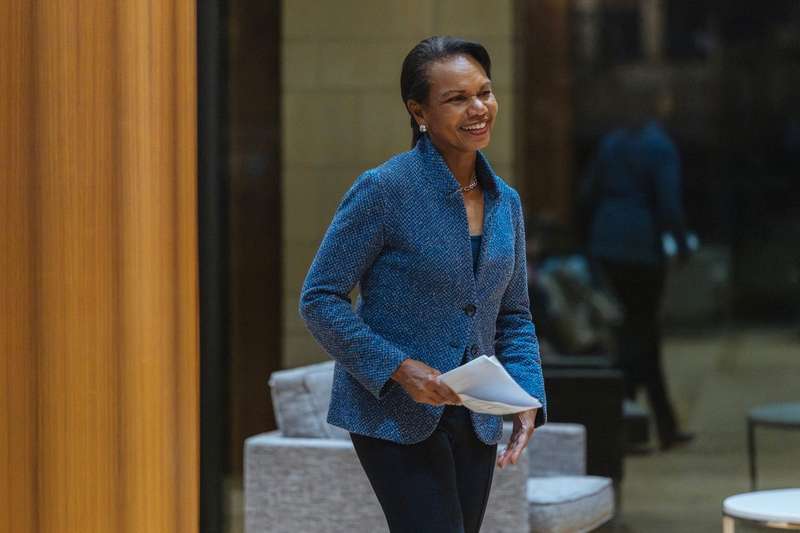 Condoleezza Rice, director of Stanford's Hoover Institution, smiles and walks across a room holding papers at a Veterans Day celebration.