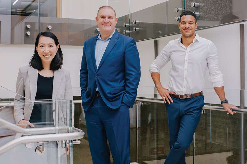 Megan Ma, Nathaniel Persily, and Julian Nyarko in professional attire pose on an office landing with glass railings.