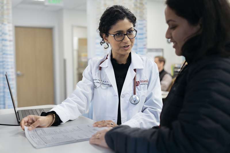 Sayantani Sindher, pediatric allergist, discusses a health issue with a patient, reviewing documents at a medical facility.