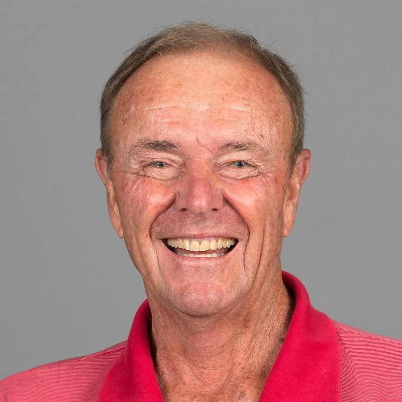 Stanford men’s tennis head coach Dick Gould smiling warmly at the camera for a profile picture against a gray background.