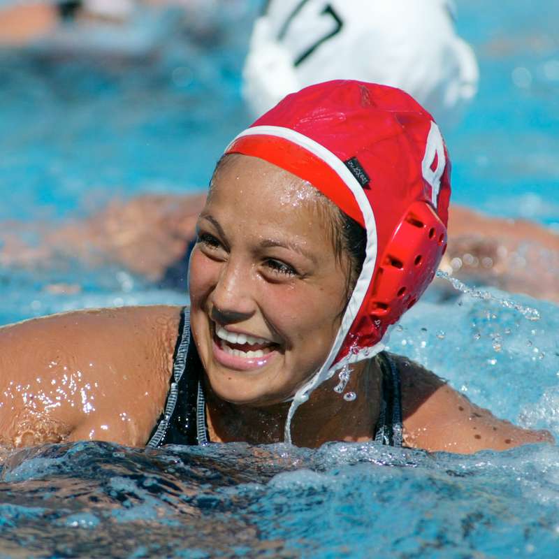Brenda Villa wearing Cardinal water polo gear and smiling as she swims through the water.