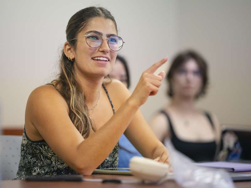 A student actively participates in a classroom discussion, pointing as she shares her thoughts.