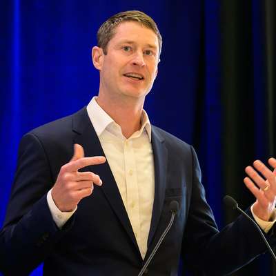 Jack Baker in a suit gestures while presenting at a lectern.