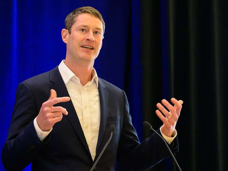 Jack Baker in a suit gestures while presenting at a lectern.