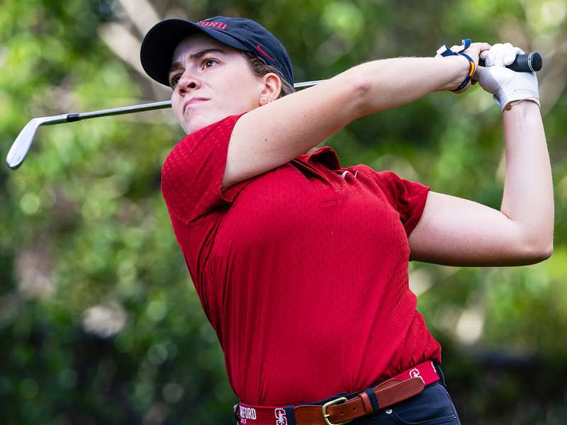 Paula Martin Sampedro swings a club on the course, wearing a red polo and black pants, with greenery in the background.