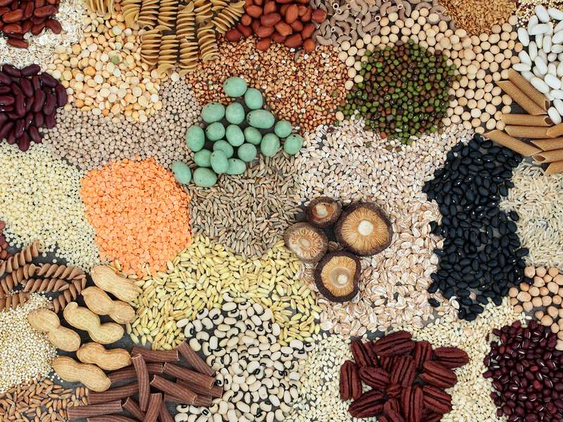 Overhead view of various legumes, grains, nuts, pasta, and dried mushrooms arranged in a colorful mosaic pattern.