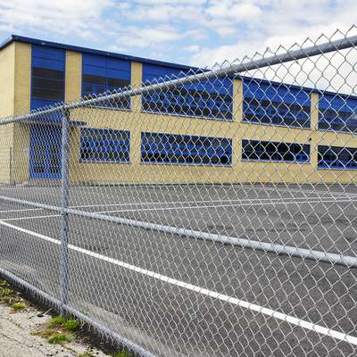 A school building with blue windows is seen behind a chain-link fence.