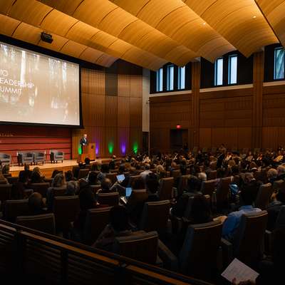 A speaker addresses a large audience at the Bio Leadership Summit in a modern auditorium with a large screen displaying the event title.