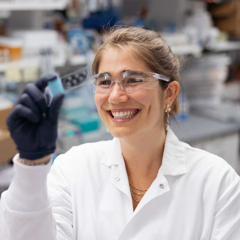 Heloise Hoffmann holds a small vial in the Stanley Qi Lab, filled with scientific equipment and materials.