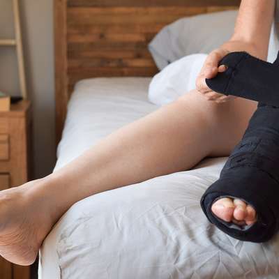 Woman sitting on bed putting on night compression wrap boot on lymphedema affected leg.