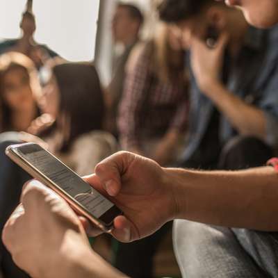 A person in a plaid shirt is using a smartphone while sitting among friends in a casual setting.