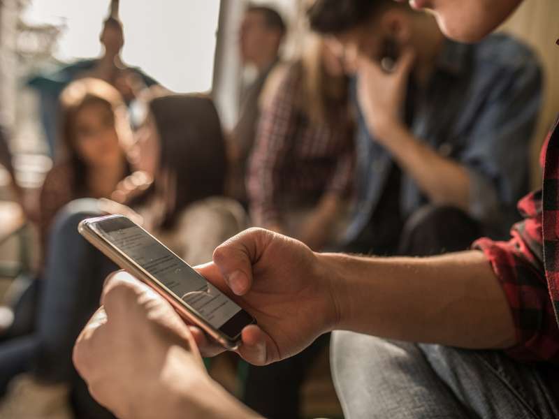 A person in a plaid shirt is using a smartphone while sitting among friends in a casual setting.