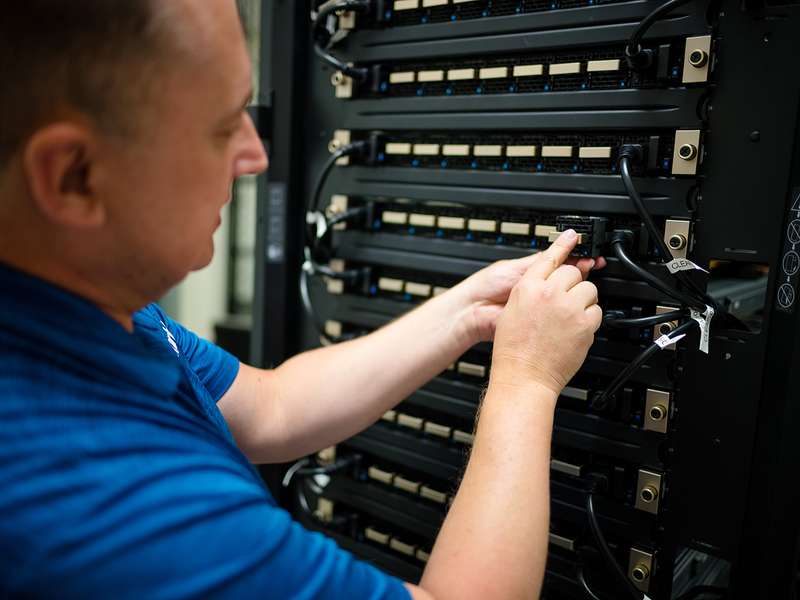 A technician connects cables on a server rack, focusing on organizing data connections in a tech environment.