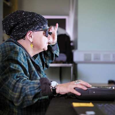 Woman wearing dark glasses uses a large-text computer monitor with assistive technology.
