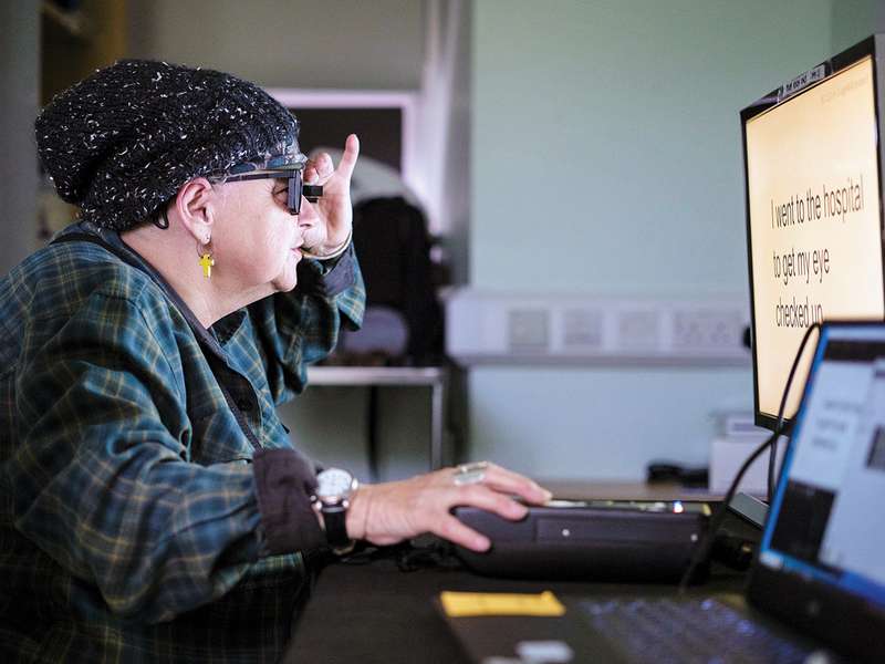 Woman wearing dark glasses uses a large-text computer monitor with assistive technology.