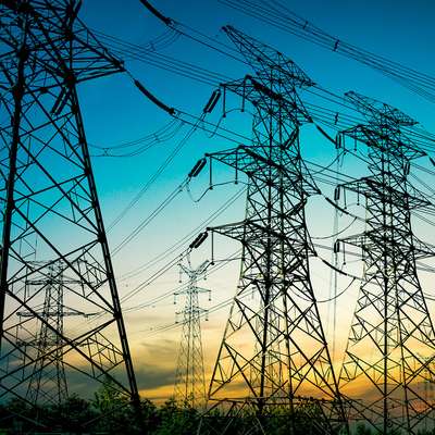 High-voltage power lines stretch across the sky during sunset, silhouetted against a vibrant blue and orange backdrop.
