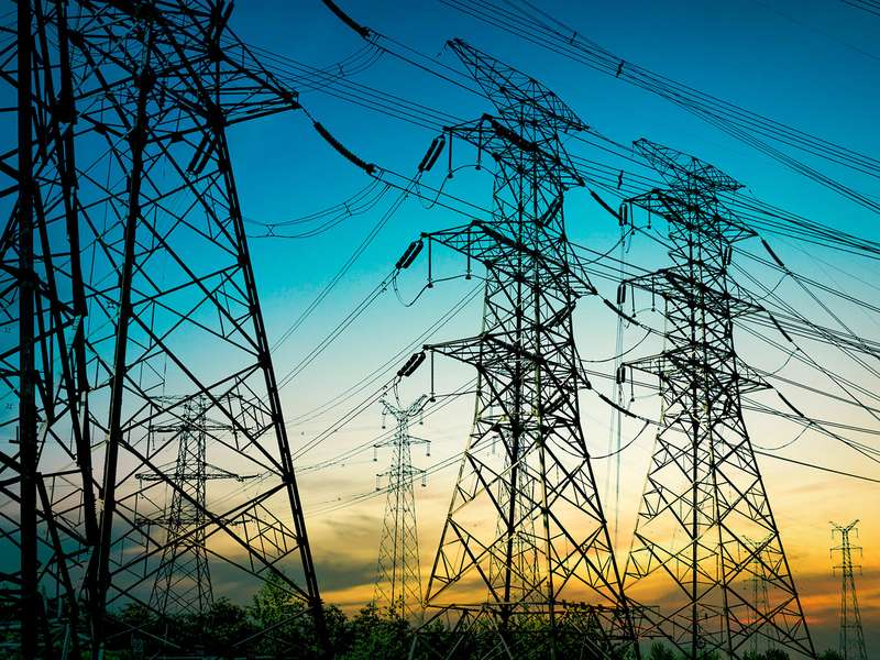 High-voltage power lines stretch across the sky during sunset, silhouetted against a vibrant blue and orange backdrop.
