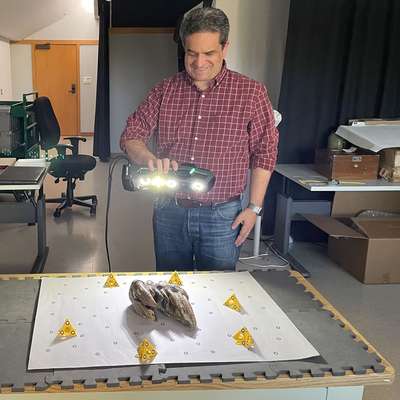 Tony Calavano smiling while scanning the fossil tooth with a handheld 3D scanner in a lab.