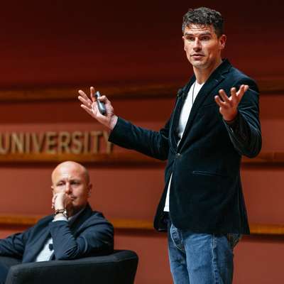 Luke Kemp gestures while presenting at a Stanford University event.