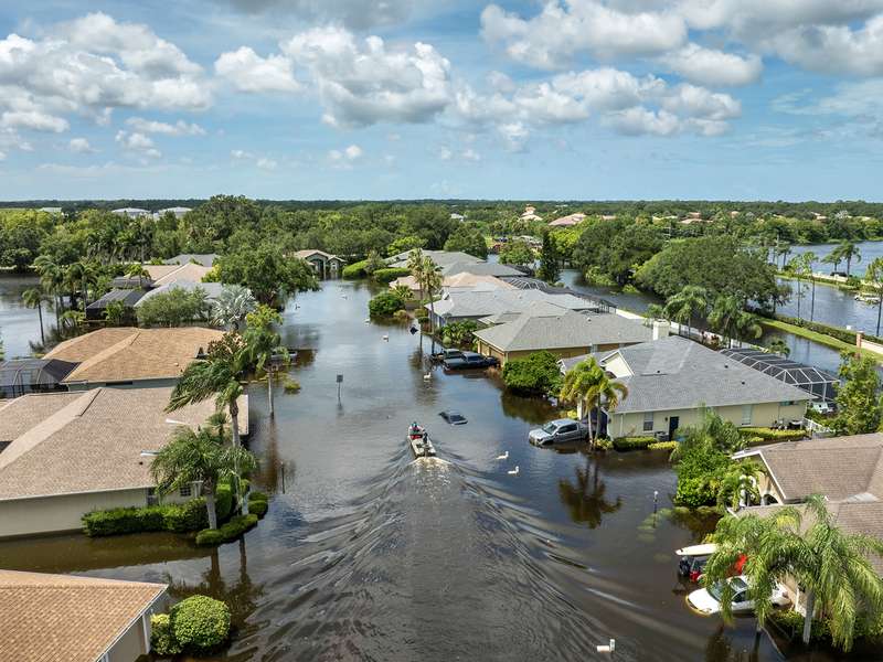 Image of people boating on rainfall flood waters between rural homes in a residential area of Sarasota, Florida, after Hurricane Debby.