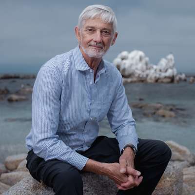 Profile photo of Stephen Palumbi sitting on rocks near the ocean.