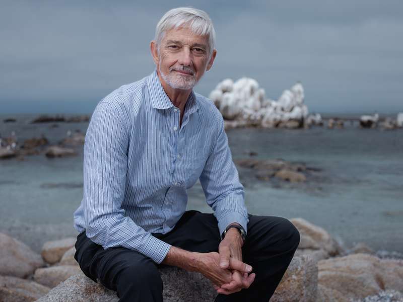 Profile photo of Stephen Palumbi sitting on rocks near the ocean.