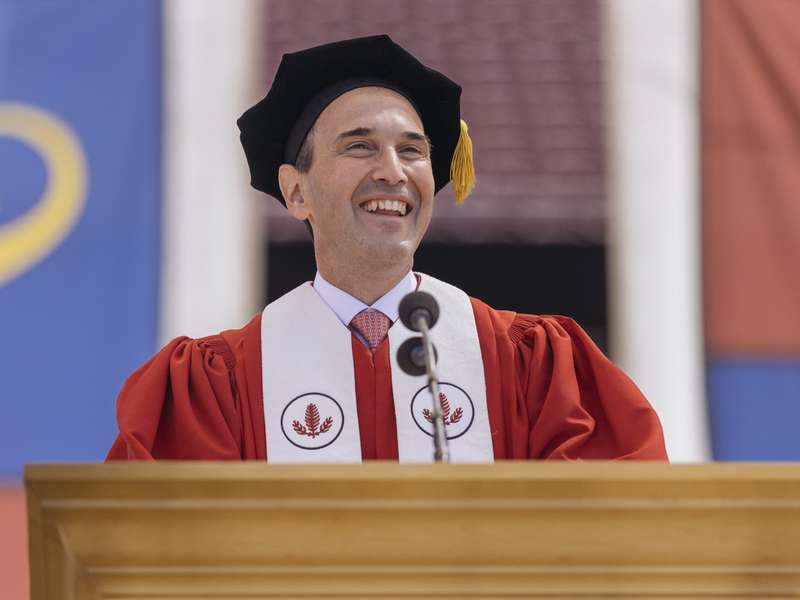 President Levin in academic regalia stands behind a podium during Commencement ceremony, addressing graduates and attendees.