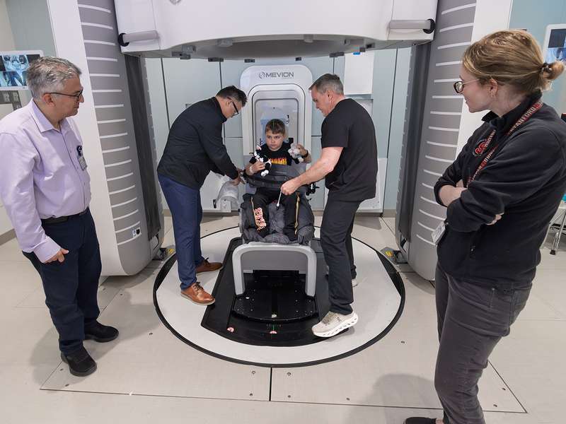 A child sits in a medical machine while adults assist, preparing for a procedure in a healthcare setting.