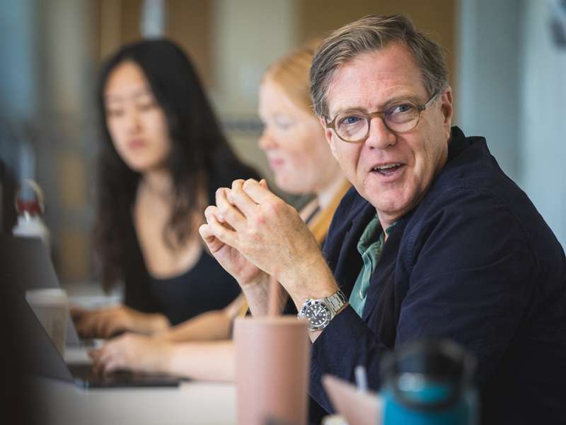 Mitchell Stevens sits at a table, looking toward the side to engage in a conversation.