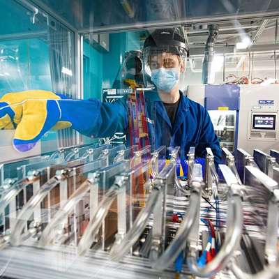 A worker in protective gear operates machinery in a cleanroom environment, focused on managing equipment with safety protocols.