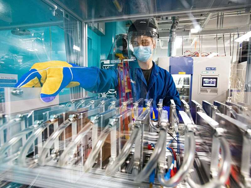 A worker in protective gear operates machinery in a cleanroom environment, focused on managing equipment with safety protocols.