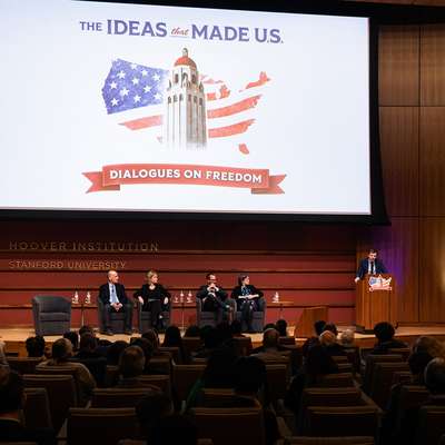 A discussion panel at Stanford University's Hoover Institution, with speakers and an audience in a modern auditorium setting.