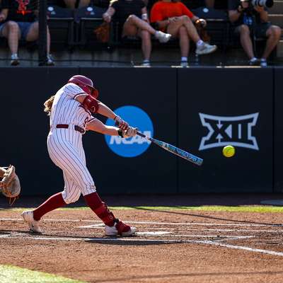 Softball player swings at a pitch as the catcher reaches for the ball.