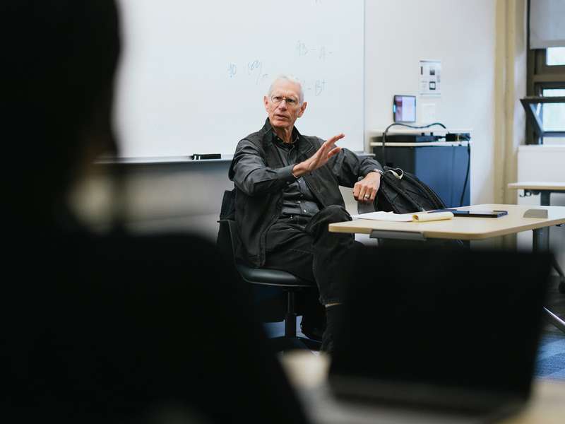 Josiah Ober gestures while speaking to students from his seat at the front of a classroom.