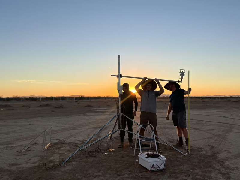 Researchers Adam Brandt, Josh Romo, and Taylor Adams set up a tripod-mounted weather sensor on a desert flat at sunset.