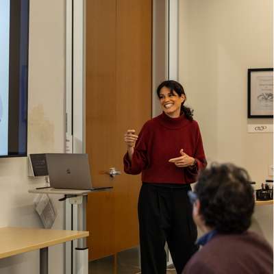 Tamar Brand-Perez gesturing toward a power point presentation during a lecture.