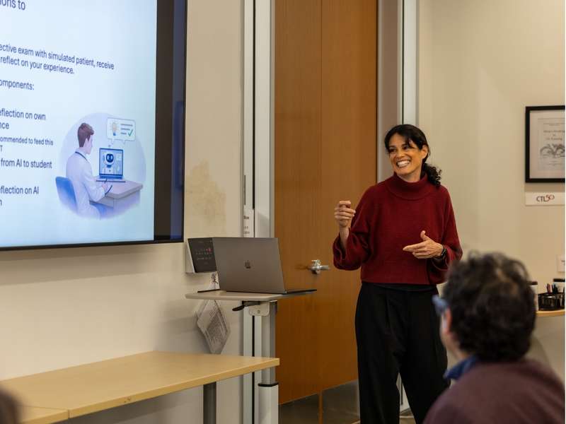 Tamar Brand-Perez gesturing toward a power point presentation during a lecture.