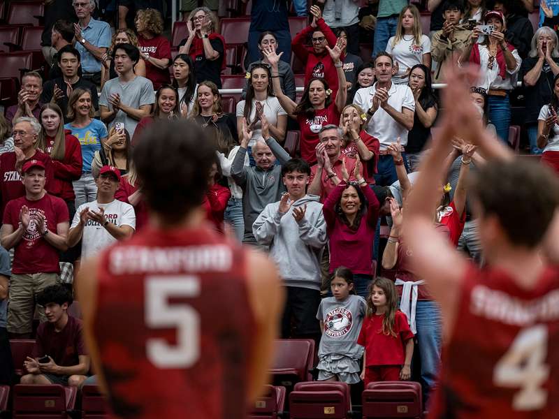Fans cheer and applaud from the stands as Stanford athletes face the crowd during a home game.