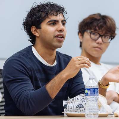 Two individuals engaged in conversation at a table with food and drinks, in a casual meeting setting.