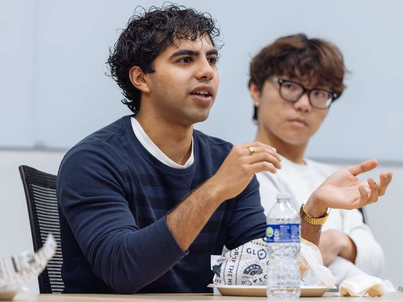 Two individuals engaged in conversation at a table with food and drinks, in a casual meeting setting.