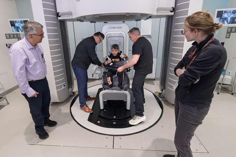 Four adults assist a child in a medical device, preparing for a procedure in a modern clinical setting.