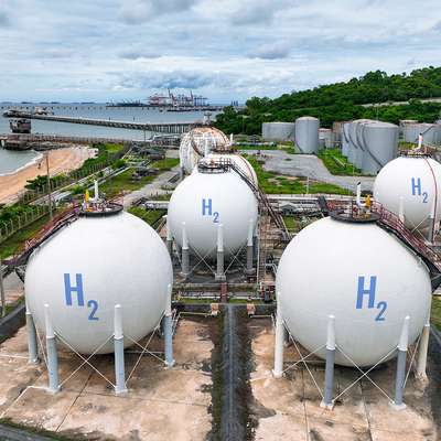 Large spherical tanks store hydrogen gas at a coastal industrial plant, with a shipping port visible in the background.