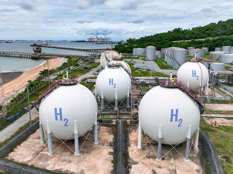 Large spherical tanks store hydrogen gas at a coastal industrial plant, with a shipping port visible in the background.
