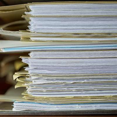 Stack of file folders stuffed with pages piled on a desk.