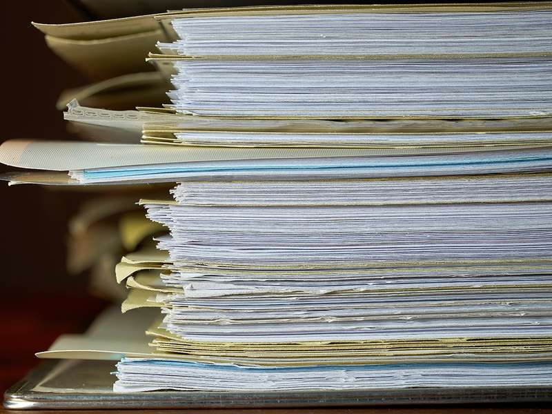 Stack of file folders stuffed with pages piled on a desk.