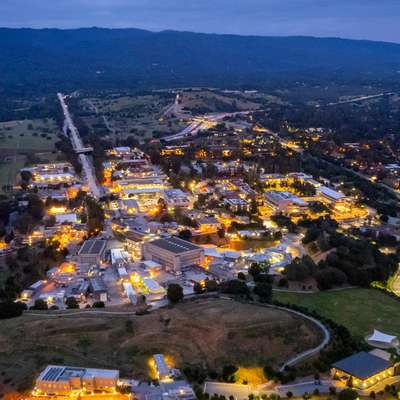 Aerial view at dusk of SLAC's facilities, with hills and a highway beyond.