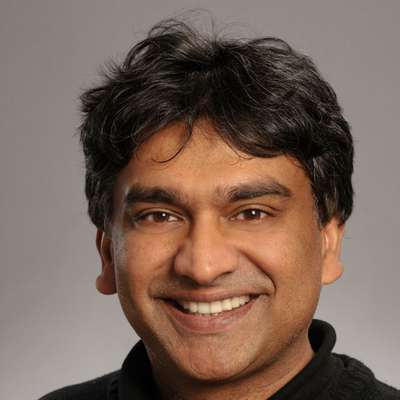 Bali Pulendran smiling into the camera against a gradient gray background.