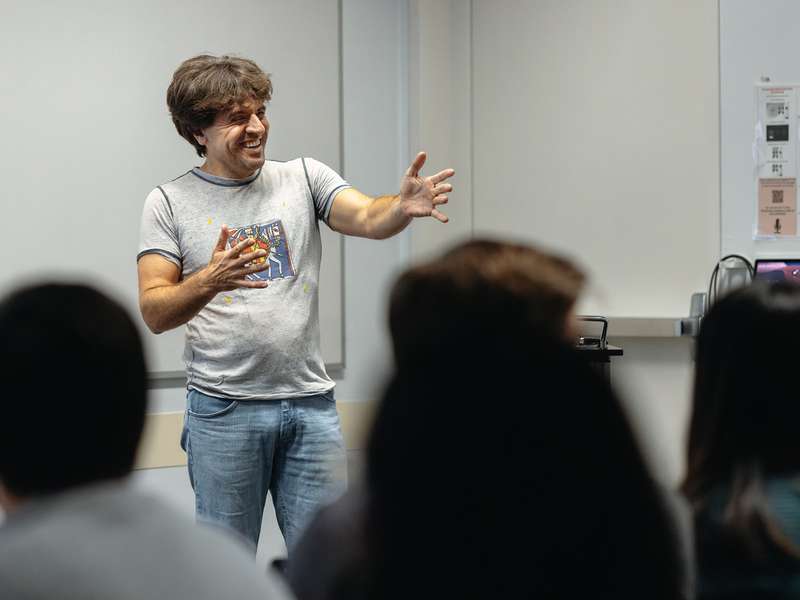 Karl Deisseroth gestures with both hands while speaking to an audience seen from behind.